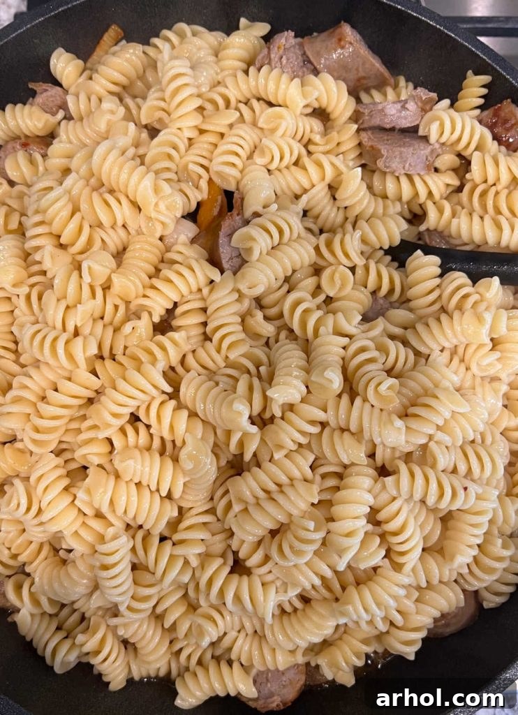 Stir cooked rotini pasta into the sausage, peppers, and onions mixture in the skillet for a combined dish.