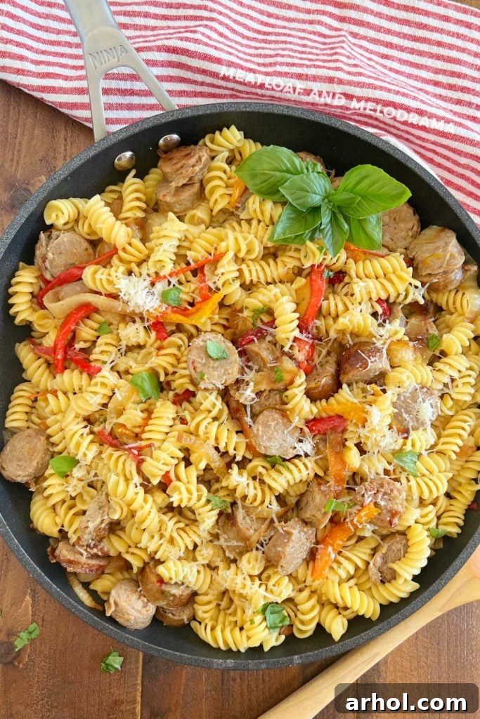 Italian sausage and peppers with rotini pasta in a skillet, garnished with fresh basil, ready to be served.