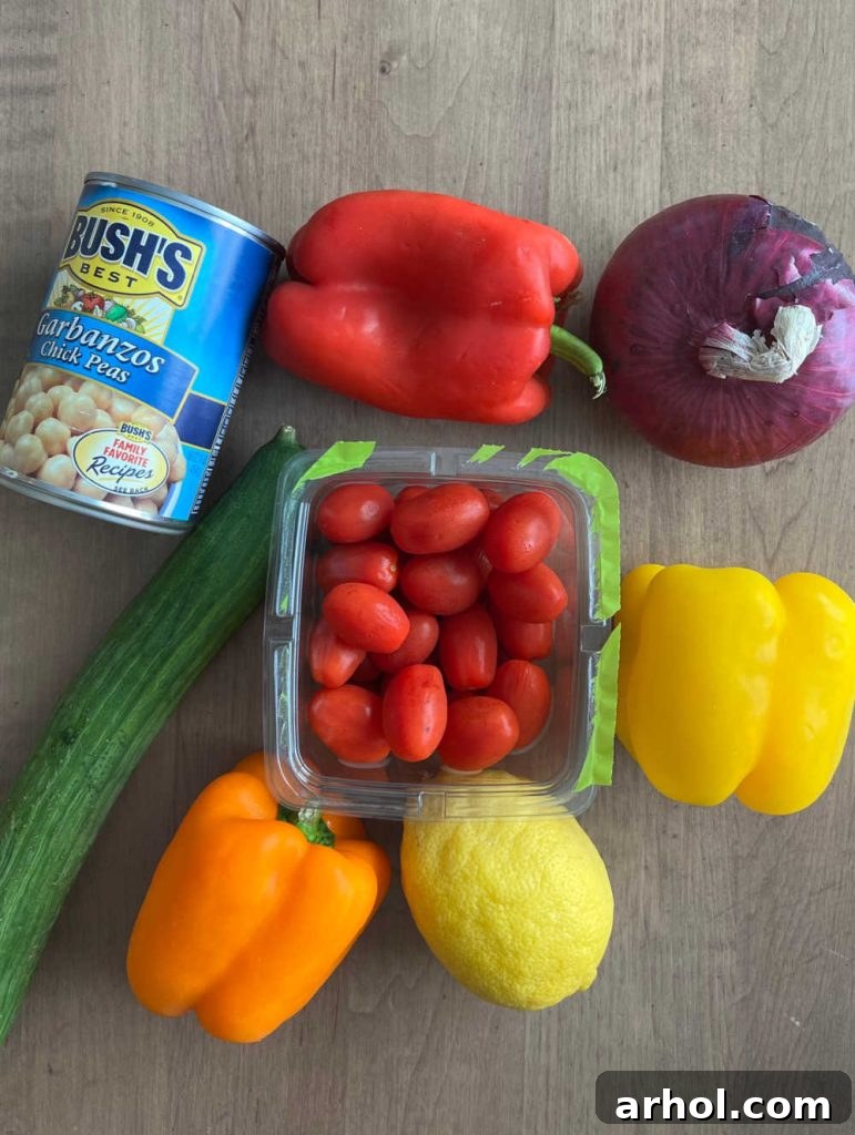 A vibrant selection of fresh ingredients laid out, including cooked garbanzo beans (chickpeas), colorful bell peppers, red onion, grape tomatoes, lemon wedges, and sliced cucumber, ready for the chickpea salad.
