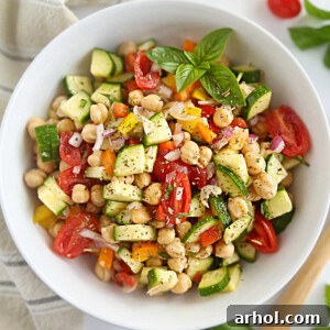 A simple chickpea salad in a white bowl with cucumbers, red onion, tomatoes, and bell peppers, ready to be served.