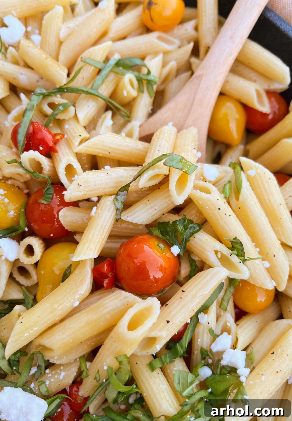 penne pasta and garden fresh tomatoes and basil in wooden spoon