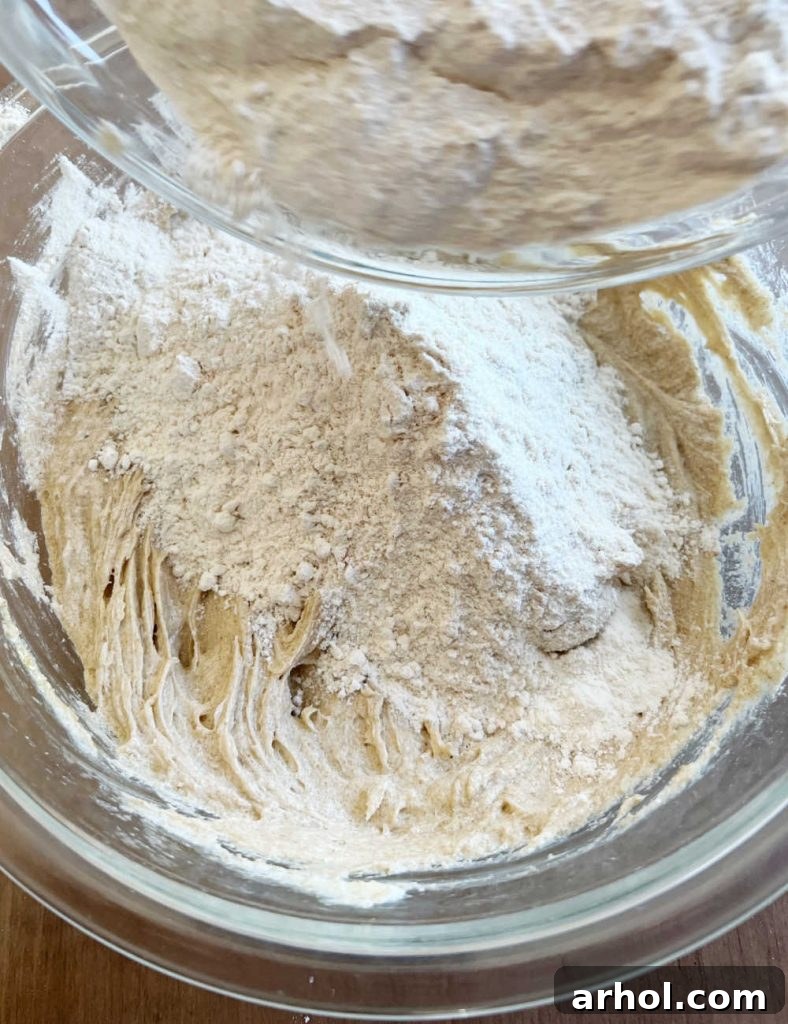 Combining wet ingredients with dry ingredients in a large mixing bowl to form cookie dough.