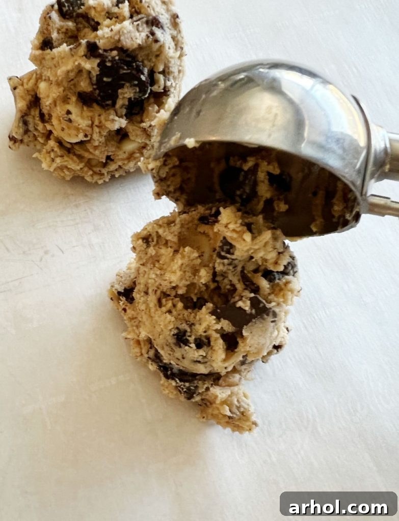 Using a cookie scoop to place evenly sized balls of cookie dough onto a baking sheet lined with parchment paper.