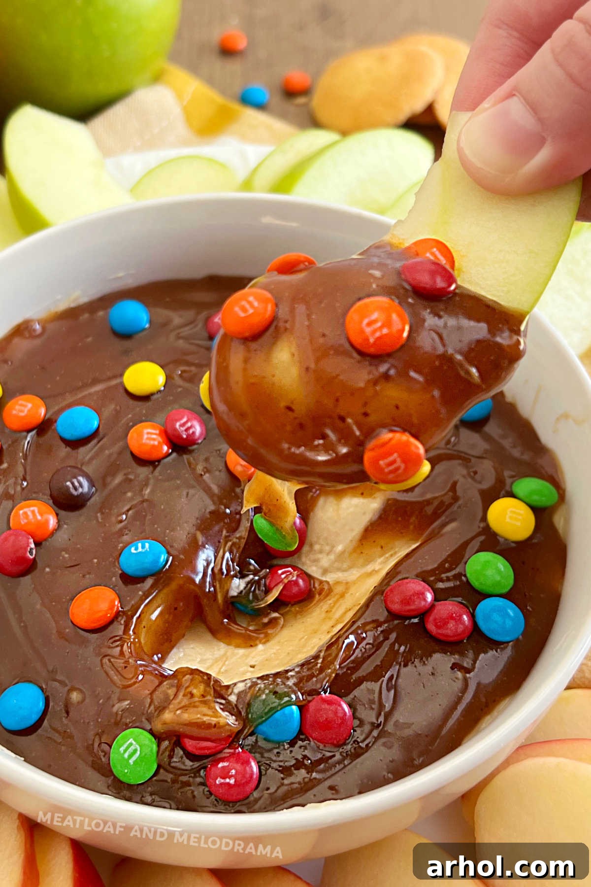 fresh apple slice dipped in caramel apple dip with mini chocolate candies