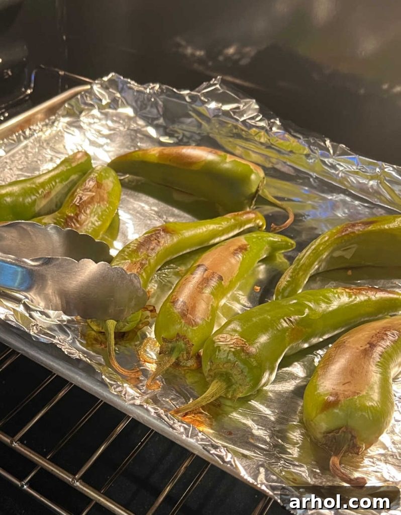 A baking sheet in the oven with Hatch chiles being rotated halfway through the roasting process, showing some blistering.