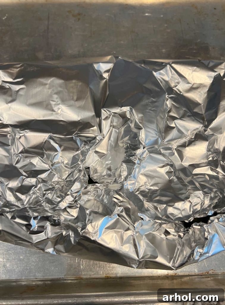 Hot roasted Hatch chiles steaming within a tightly folded aluminum foil packet on a baking sheet, to loosen their skins.