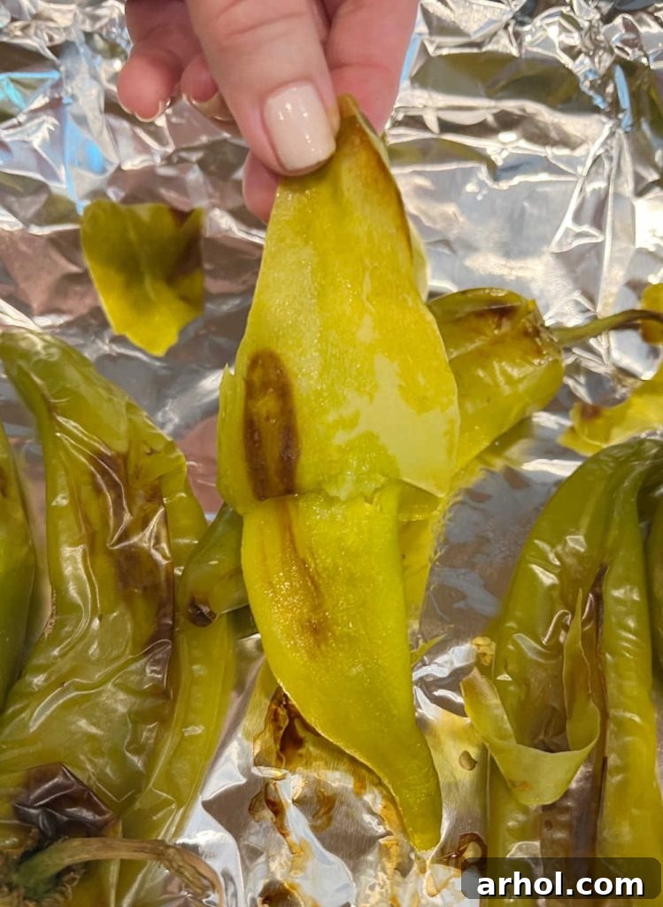 A hand gently peeling the charred skin off a roasted Hatch chile pepper, revealing the tender green flesh underneath.