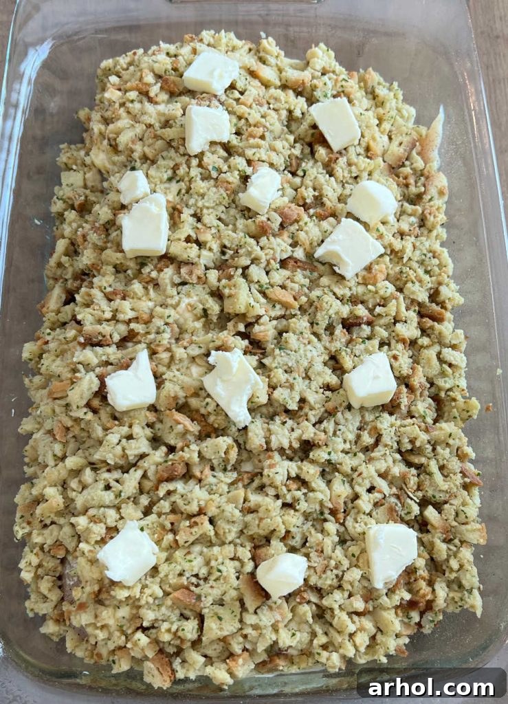 Small cubes of butter meticulously placed over the top layer of stuffing in a casserole dish, ready for baking.
