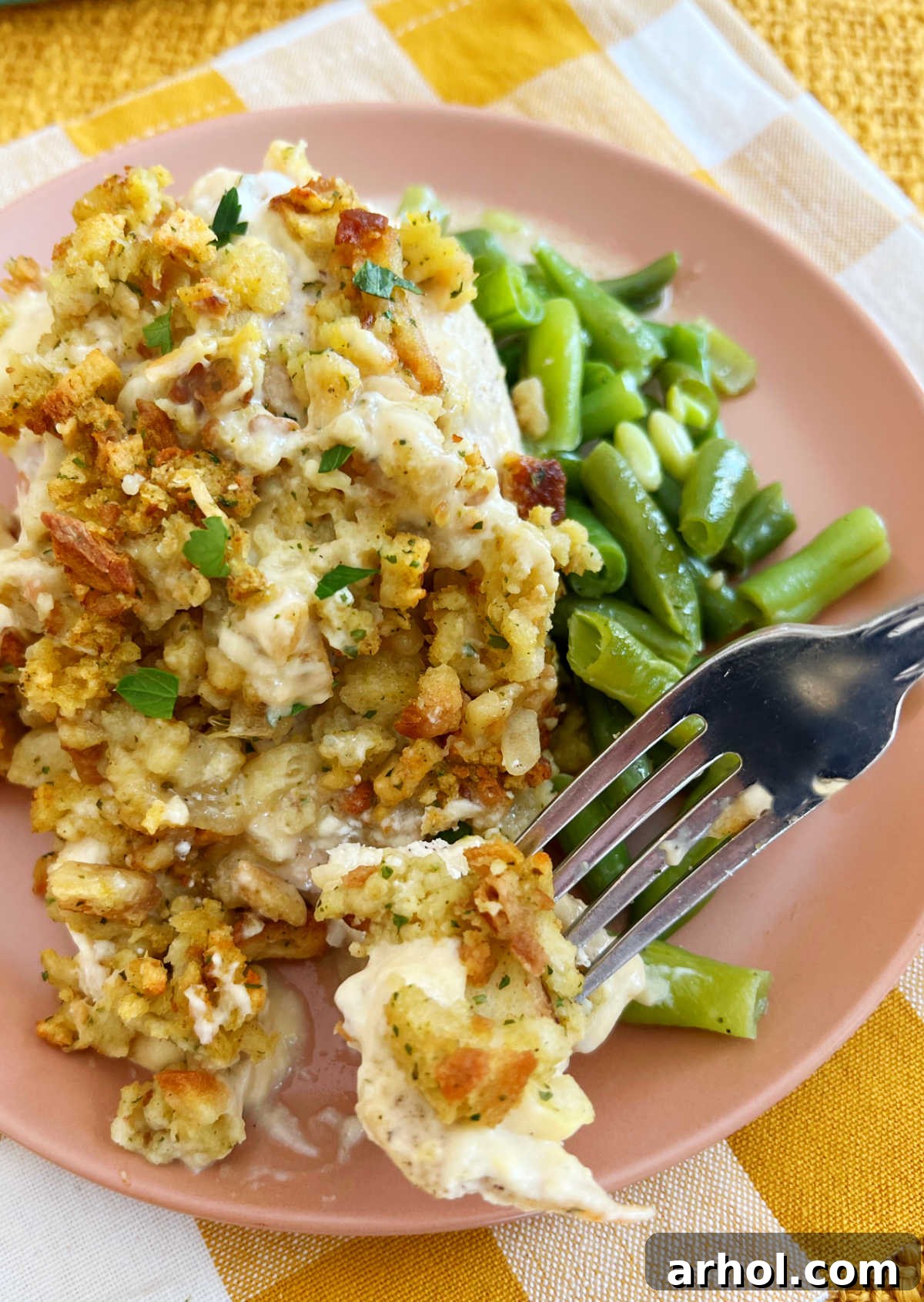 A fork lifting a delicious bite of chicken stuffing bake, showcasing the crispy topping, creamy chicken, and a side of fresh green beans.
