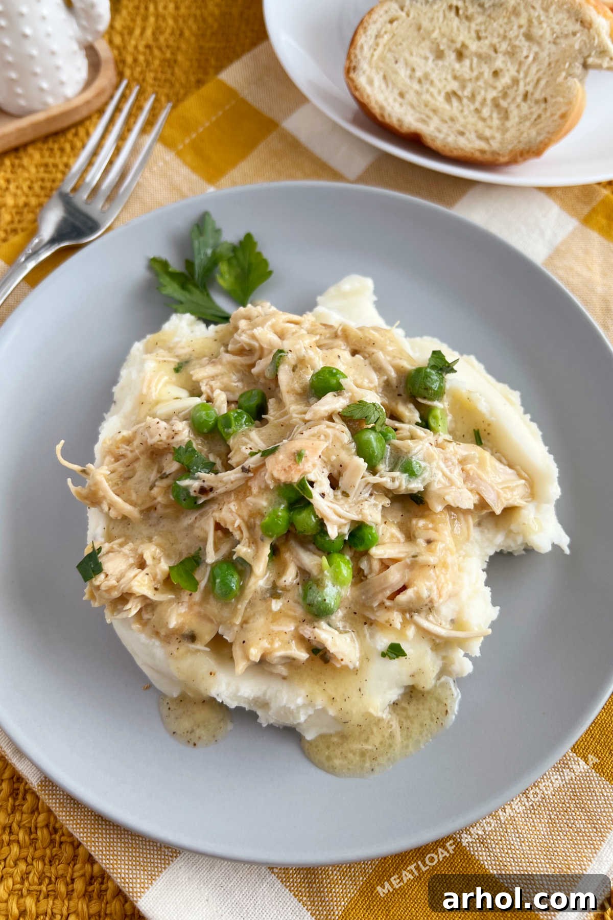 crockpot chicken and gravy over mashed potatoes with peas on the table
