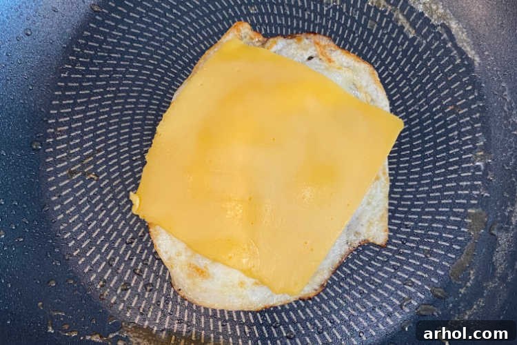 Golden Sausage Egg Cheese Sandwich 4 Fried egg with a slice of American cheese melting in a pan, ready for assembly