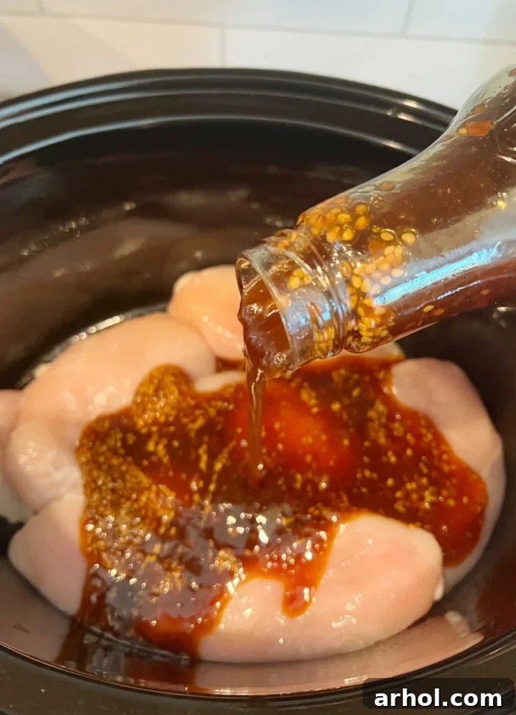Pouring teriyaki sauce over raw chicken breasts in a slow cooker