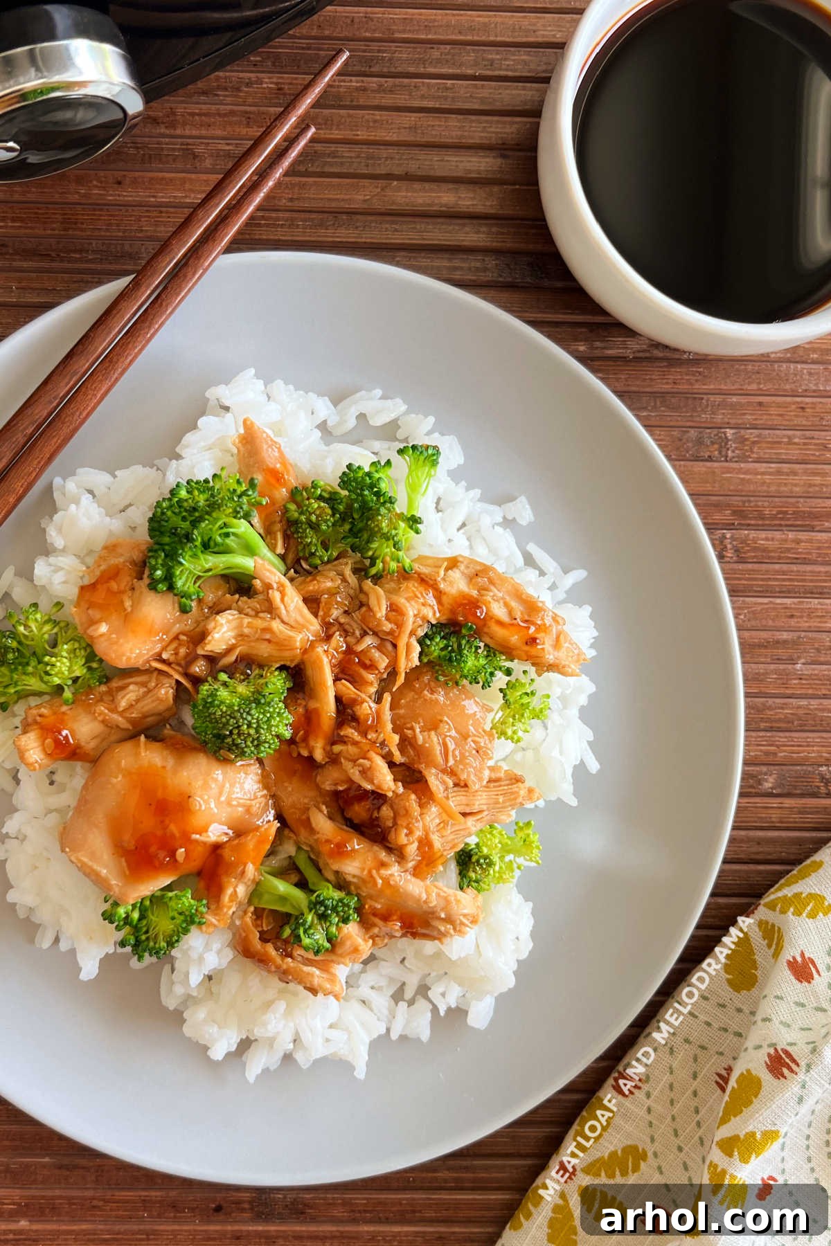 Close-up of slow cooker teriyaki chicken and broccoli served over rice, garnished with sesame seeds.