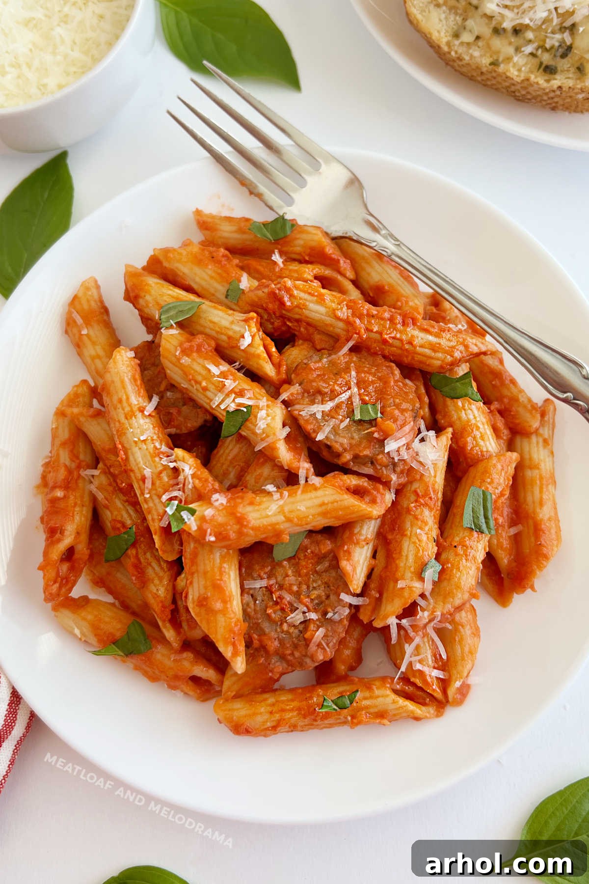 Penne alla Vodka with Italian sausage, Parmesan cheese and fresh basil, garnished on a white plate.