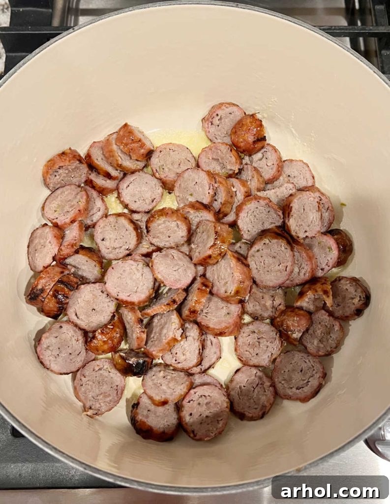 Sliced Italian sausage with onions in a Dutch oven, starting to brown.