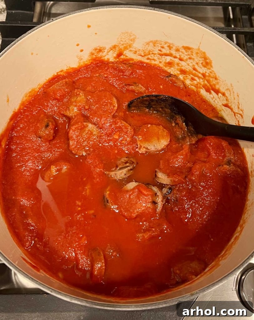 Italian sausages simmering in crushed tomatoes in a pot.