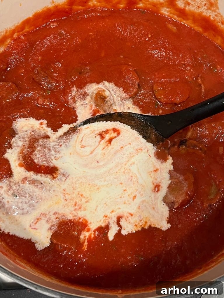 Heavy cream being stirred into the tomato sauce with vodka.