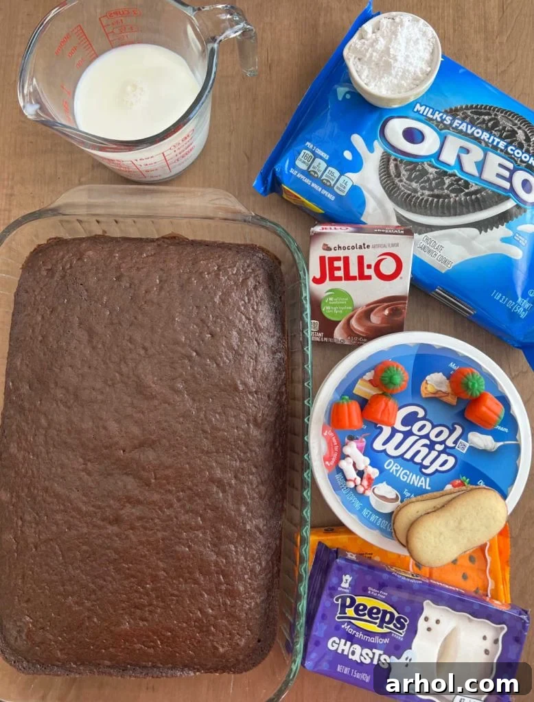 A flat lay photograph showcasing all the primary ingredients for Halloween Dirt Cake, including chocolate cake mix, milk, instant chocolate pudding mix, whipped topping, powdered sugar, Oreo cookies, and various Halloween candies for decoration.