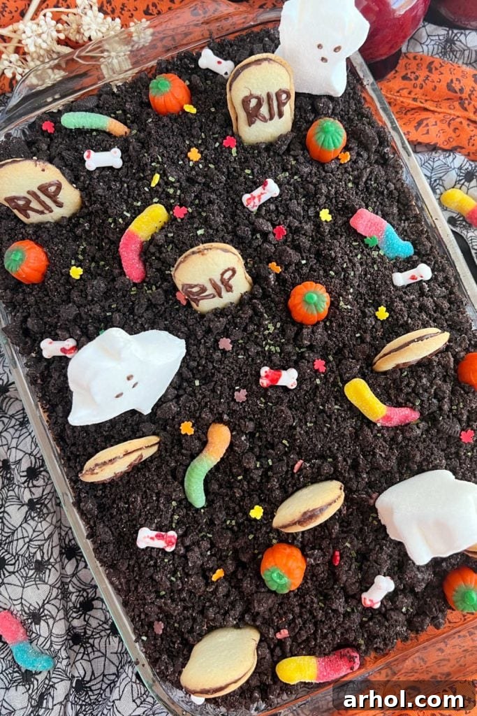 A captivating shot of the Halloween graveyard cake in its baking pan, partially decorated with Milano cookie gravestones and an assortment of colorful Halloween candies, ready for final touches.