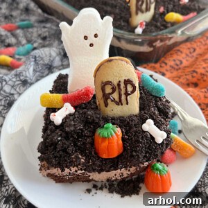 A square image of Halloween Dirt Cake, richly decorated with crushed Oreos, playful gummy worms, classic Milano cookie gravestones, and an adorable marshmallow ghost, all presented on a plate.