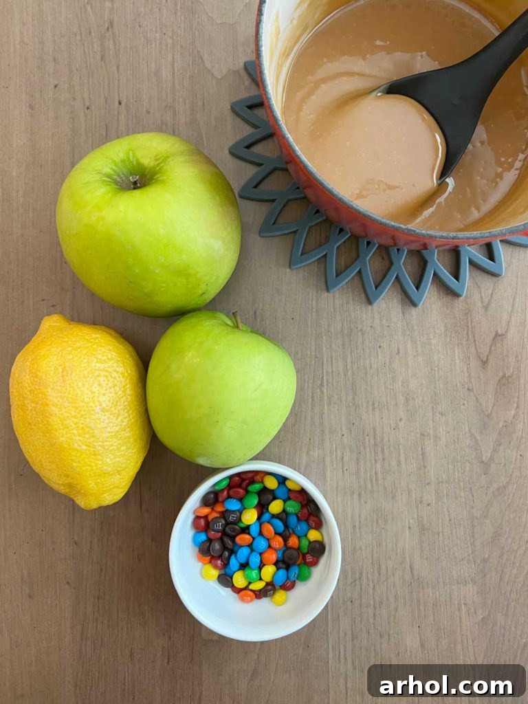 Caramel Apple Nacho Delight 3 A beautifully composed flat lay image showcasing the core ingredients for caramel apple nachos: vibrant green Granny Smith apples, a bottle of lemon juice, a jar of rich caramel sauce, and a colorful bowl of mini M&M's candies.