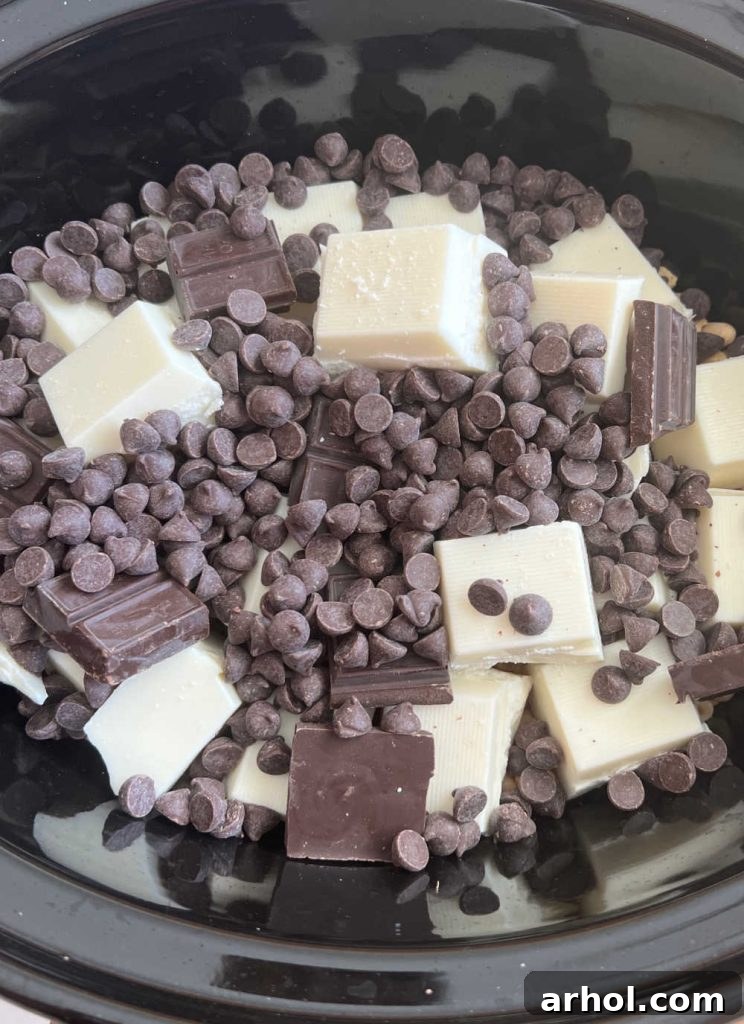 Layers of almond bark, German chocolate, and semi-sweet chocolate chips placed on top of peanuts in a crockpot.