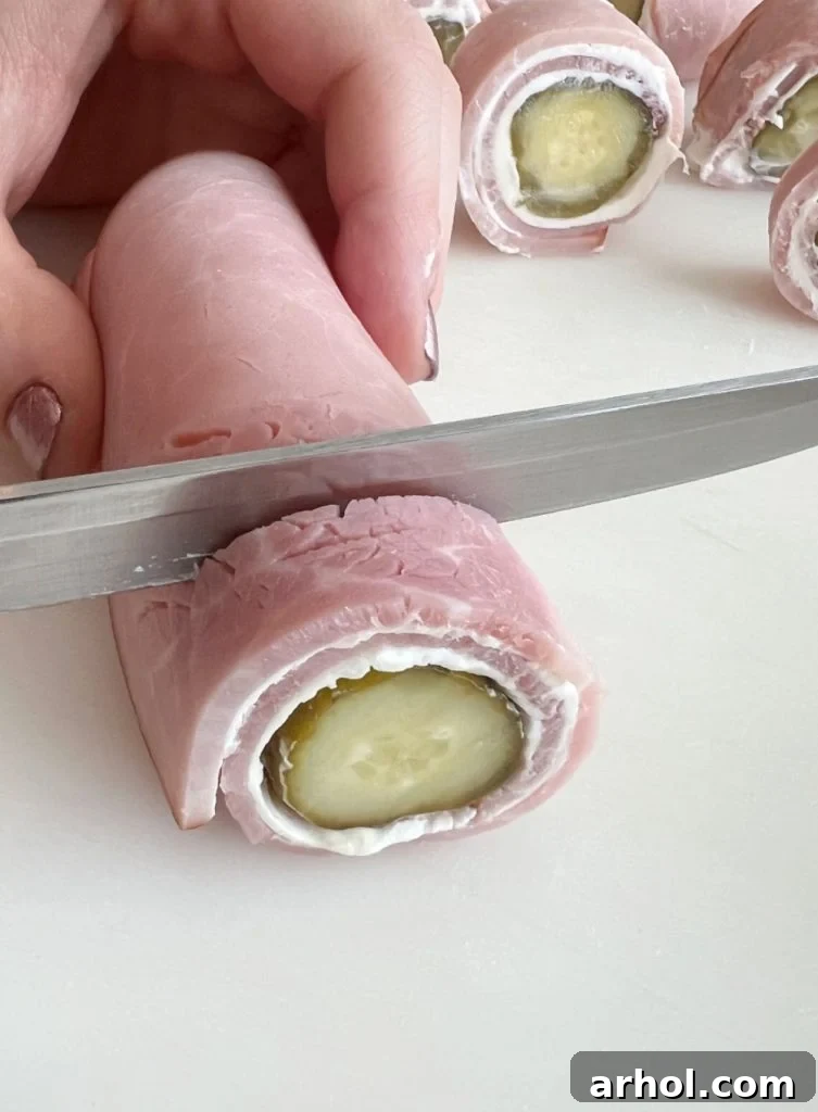A sharp knife slicing a ham and cream cheese roll-up into perfectly portioned rounds.
