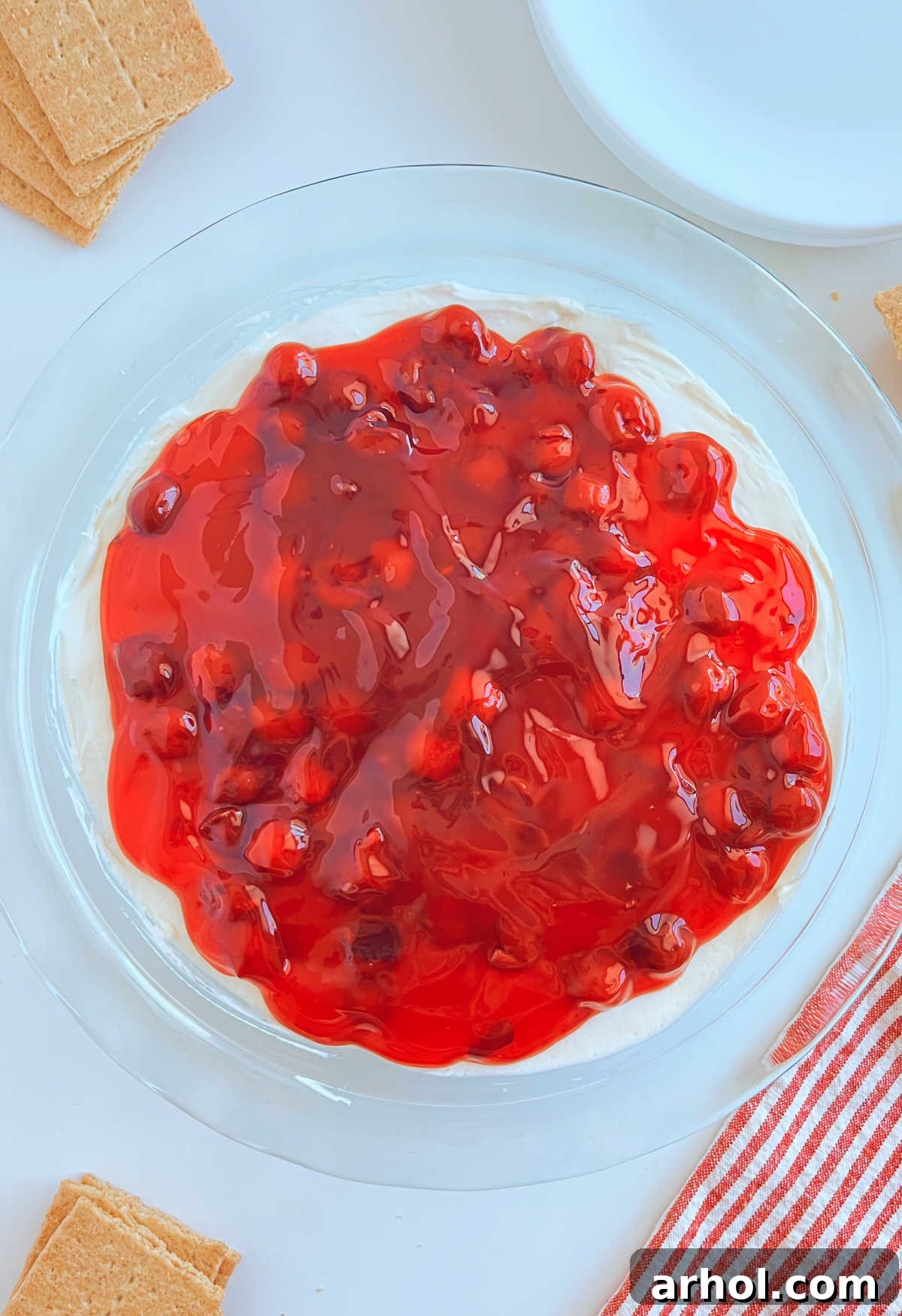 Luscious Cherry Cheesecake Dip 7 Close-up of cherry cheesecake dip in a glass pie dish, topped with glossy red cherry pie filling, ready to be served.