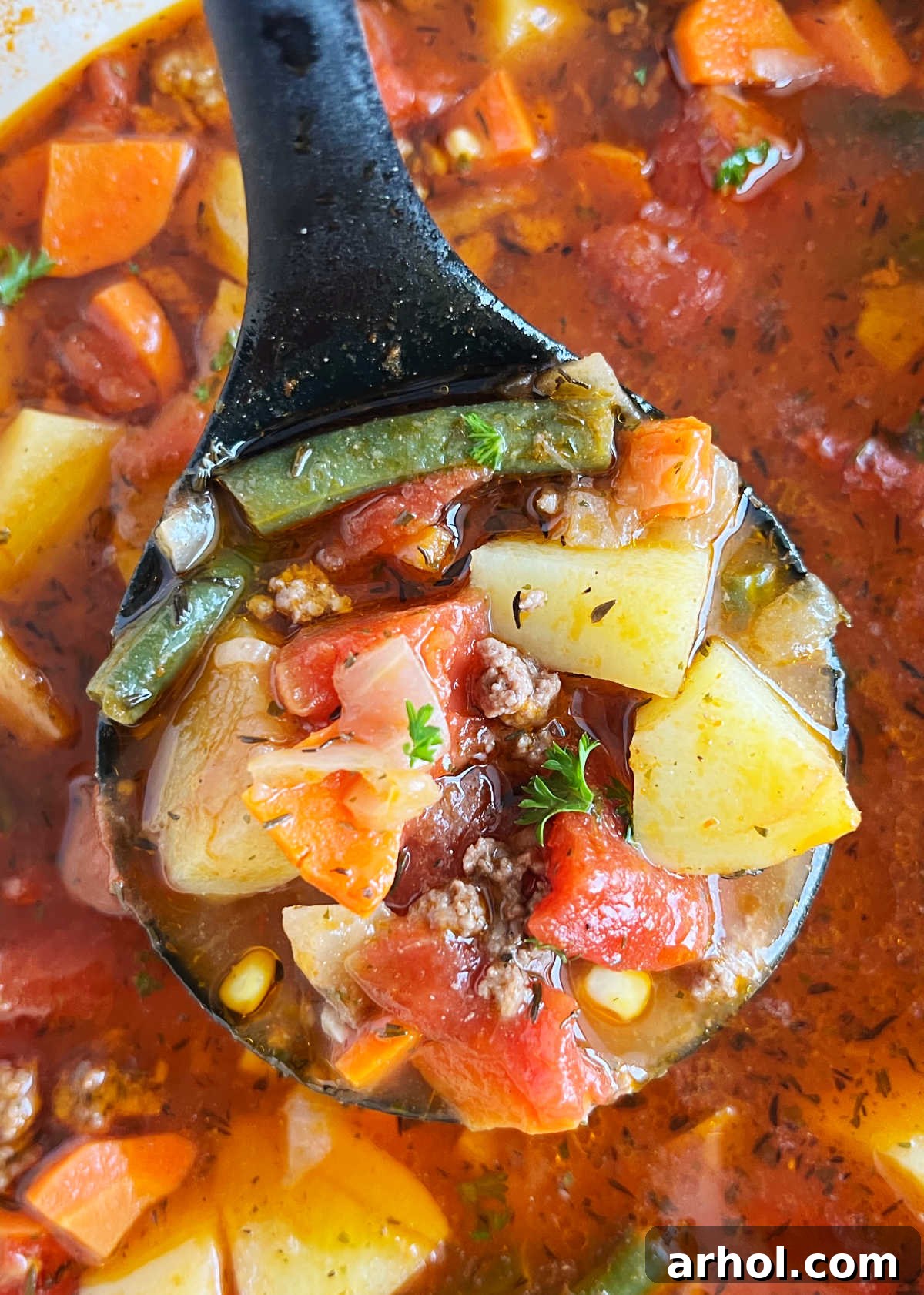 Comforting Ground Beef and Veggie Soup 7 Ladle with steaming ground beef vegetable soup held over a Dutch oven, ready to be served