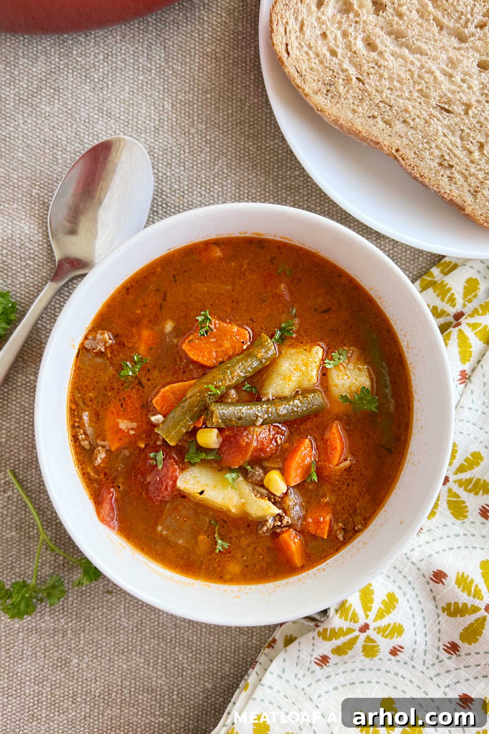 Comforting Ground Beef and Veggie Soup 8 A comforting bowl of ground beef vegetable soup on a rustic wooden table, garnished with fresh herbs