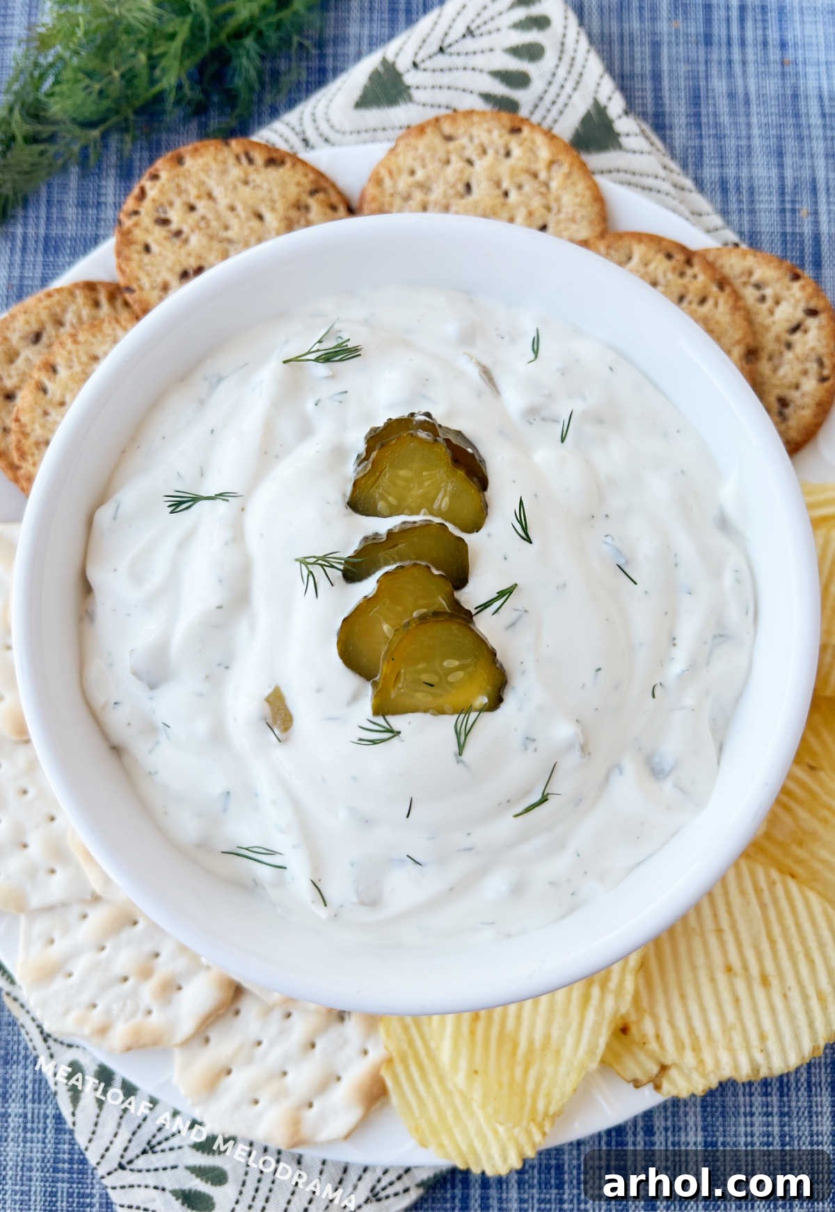 Dill pickle dip in a white bowl with potato chips and crackers, ready to serve