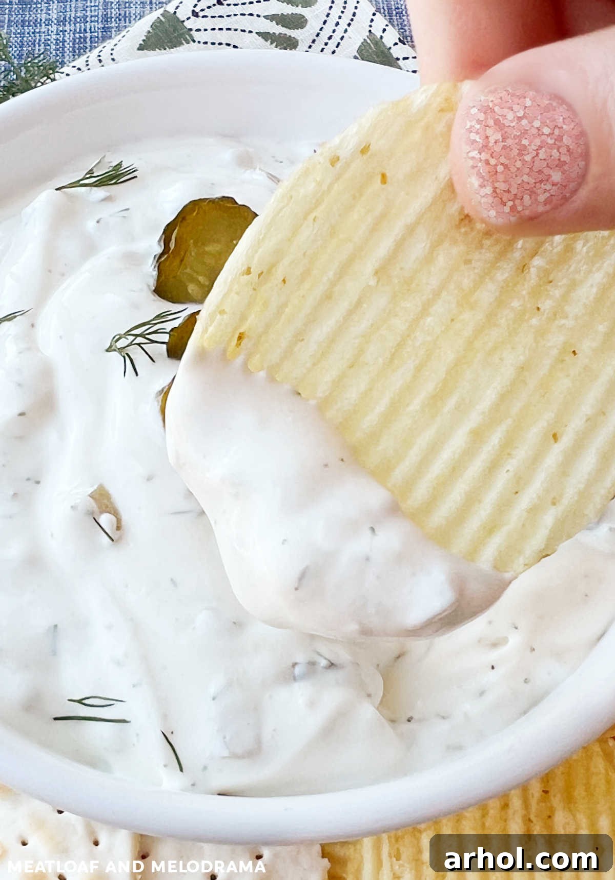 Dipping a potato chip into a bowl of creamy dill pickle dip