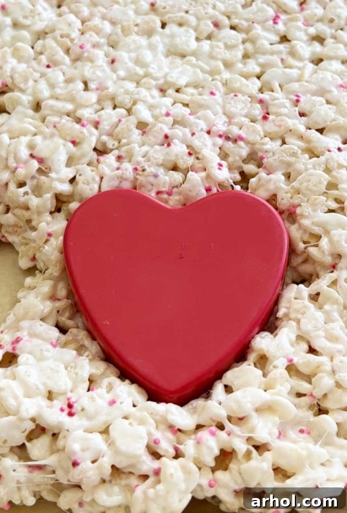 Using a heart-shaped cookie cutter to cut out heart shapes from a sheet of Rice Krispie Treats