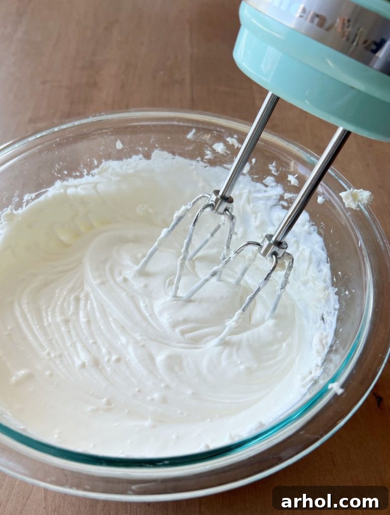 Blending softened cream cheese and sour cream together with an electric hand mixer in a large mixing bowl until smooth and creamy.