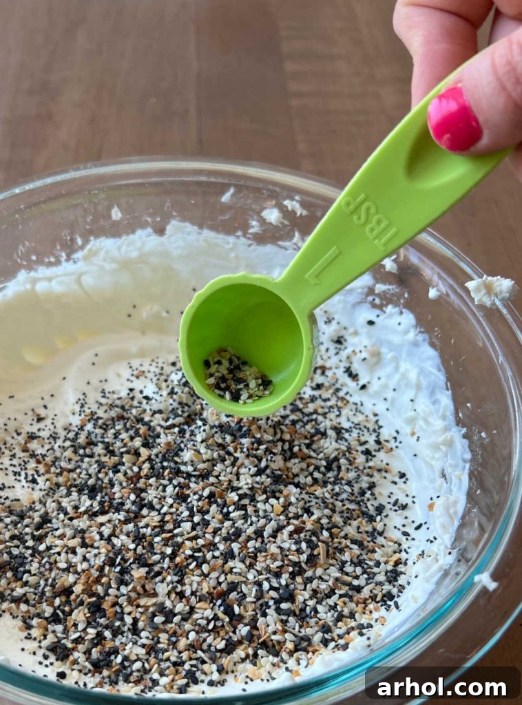 Sprinkling everything bagel seasoning blend into the creamy sour cream and cream cheese mixture.