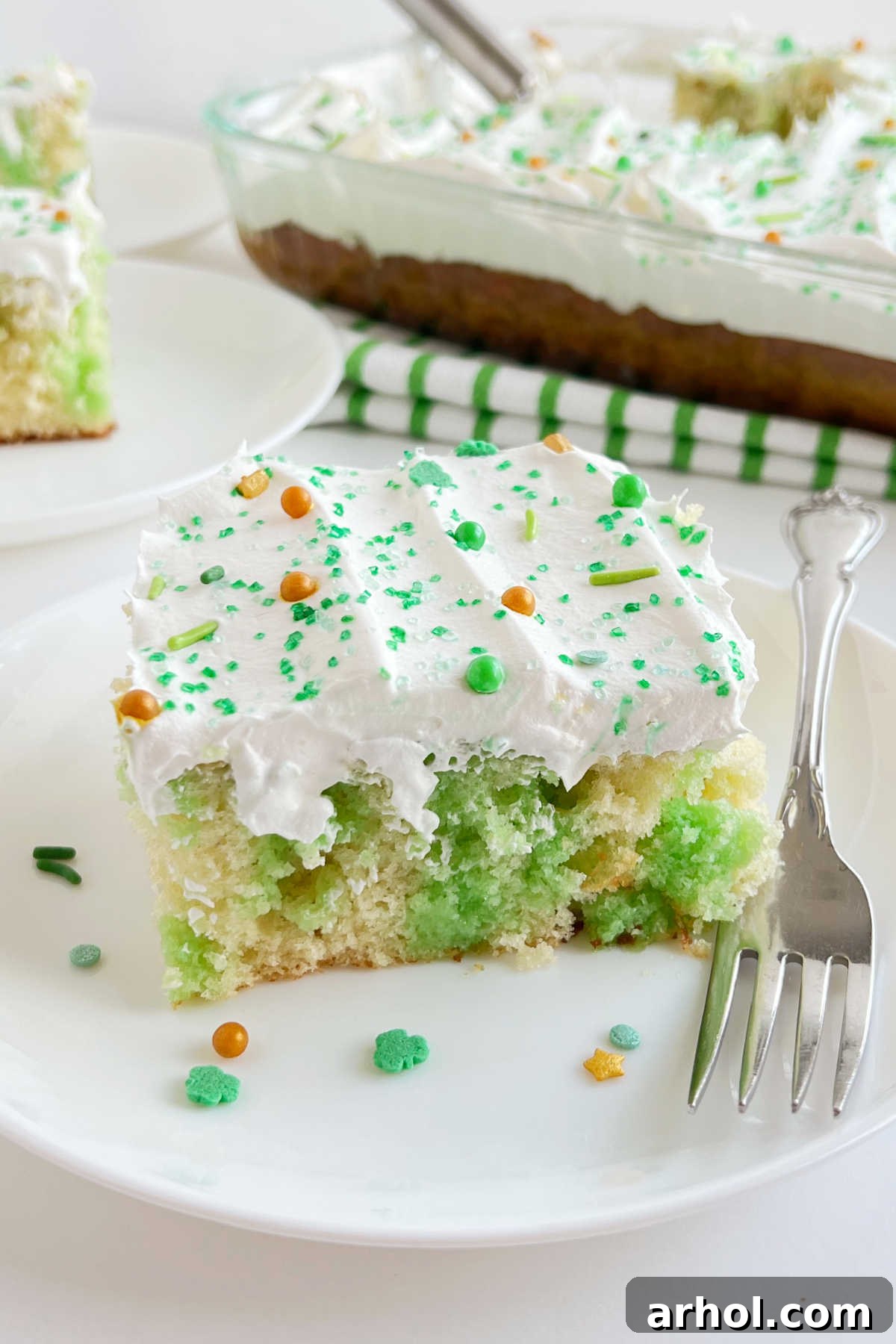 Lime Jello Poke Cake with a fluffy whipped topping and festive St. Patrick's Day sprinkles, ready to be served.