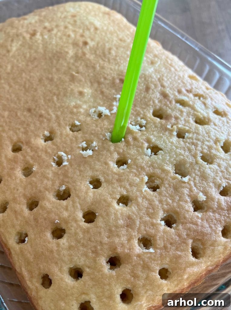 Poking holes into the warm cake using a large drinking straw, preparing it for the lime Jell-O mixture.