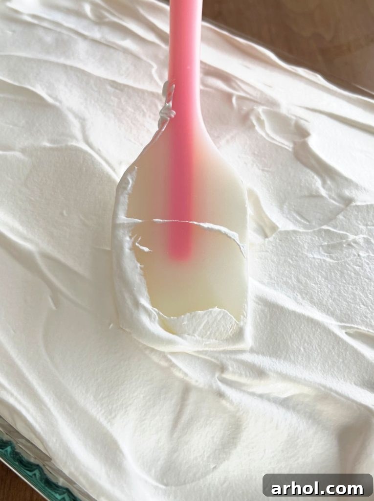 Spreading a generous layer of creamy Cool Whip whipped topping evenly over the chilled Lime Jello Poke Cake.