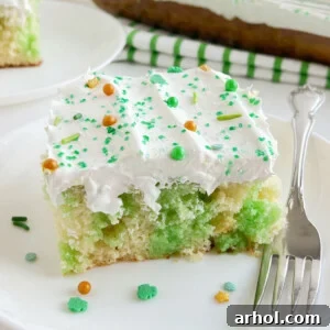 A slice of Lime Jello Poke Cake with festive St. Patrick's Day sprinkles on a white plate.