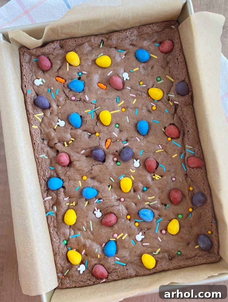 Mini Egg Magic Brownies 6 Freshly baked fudgy brownies in a baking dish, adorned with colorful Cadbury mini eggs and festive spring sprinkles.