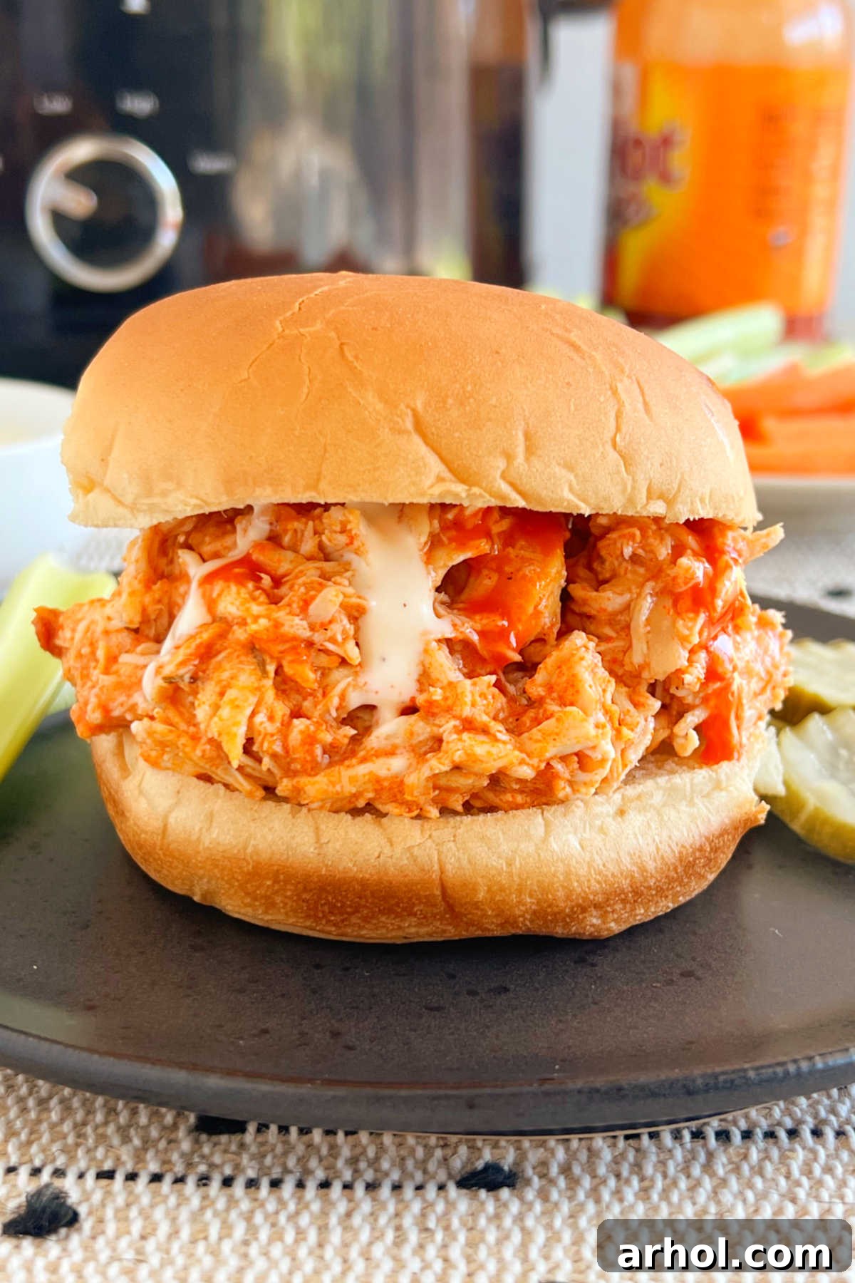 crock pot buffalo chicken sandwiches with shredded chicken on a bun, topped with ranch dressing