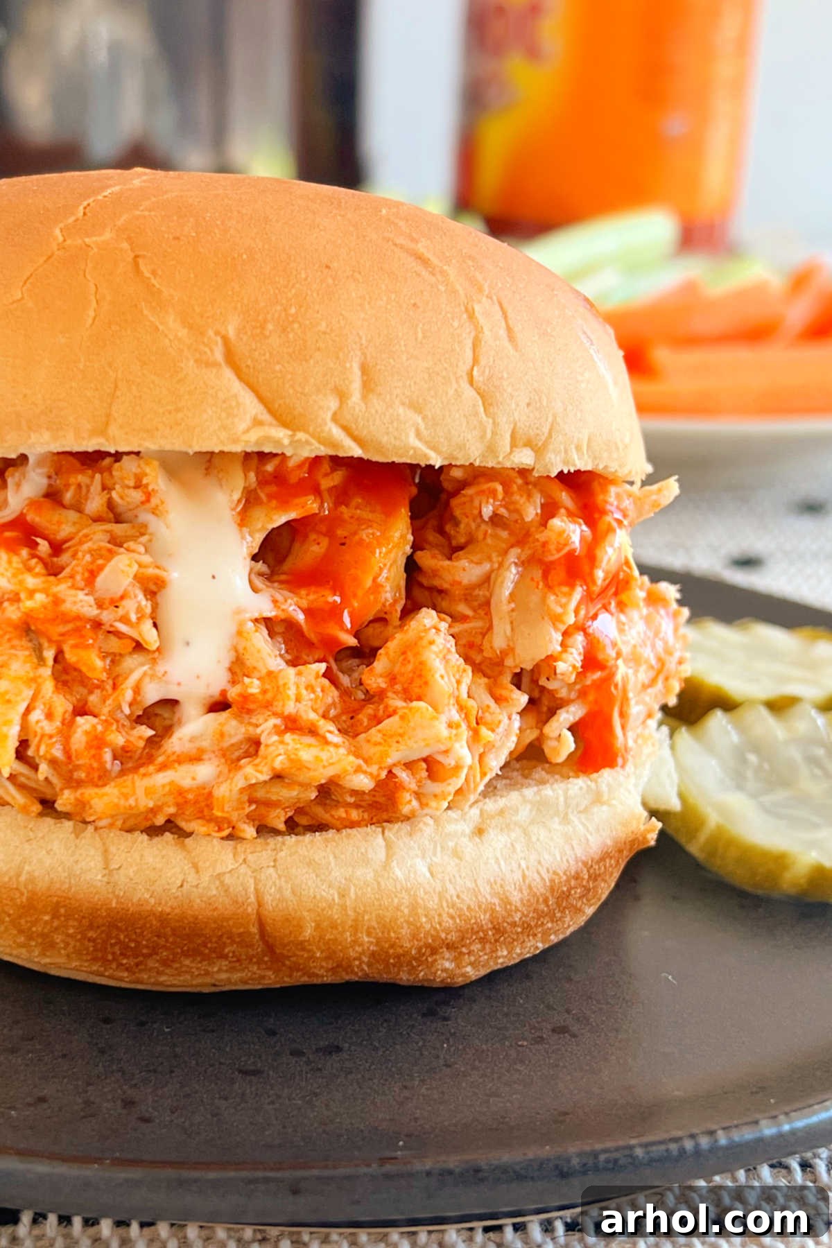 pulled crock pot buffalo chicken sandwich with ranch dressing on plate, served with celery and carrot sticks