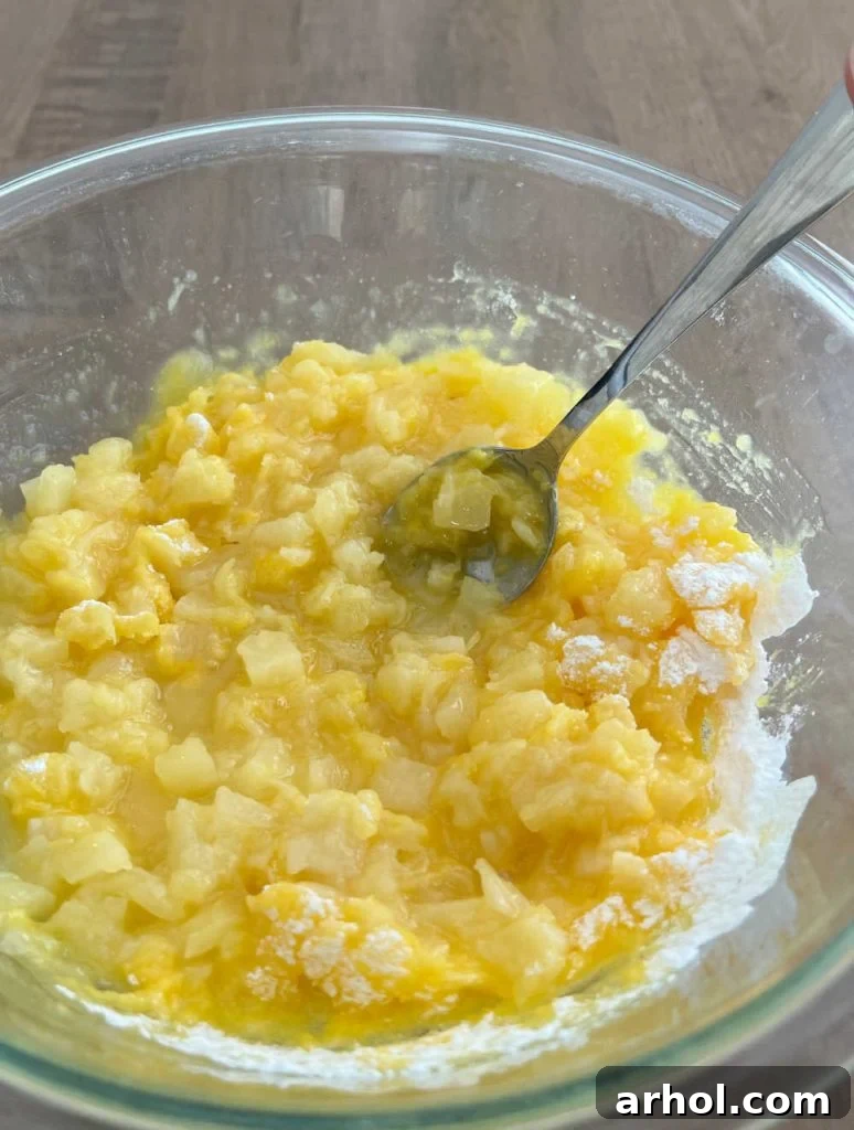 A large bowl containing dry vanilla pudding mix and undrained crushed pineapple being stirred together until well combined.