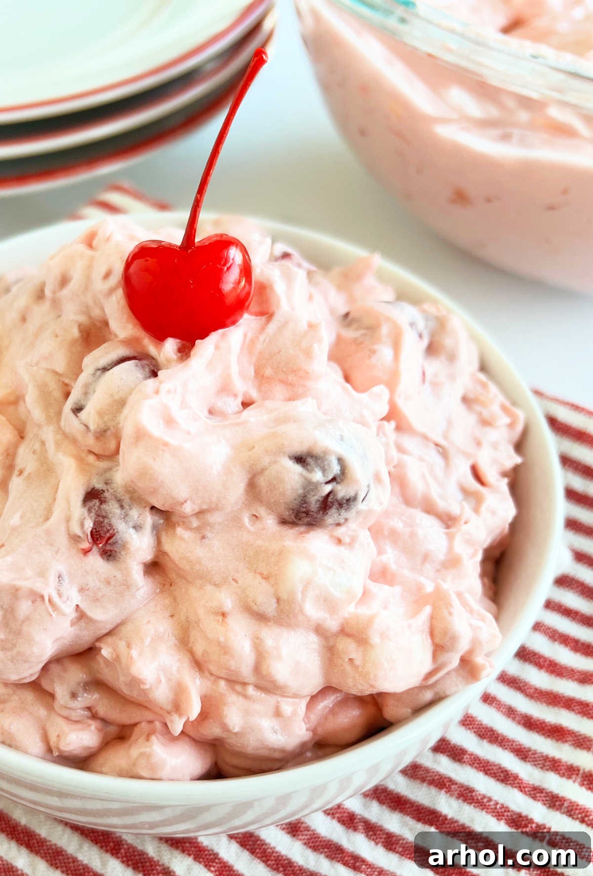 A large glass bowl filled with fluffy pink Cherry Fluff salad, topped with a few maraschino cherries and mini marshmallows, showcasing its creamy texture.