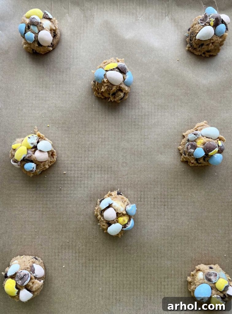 Easter cookie dough balls on a baking sheet, topped with more mini eggs