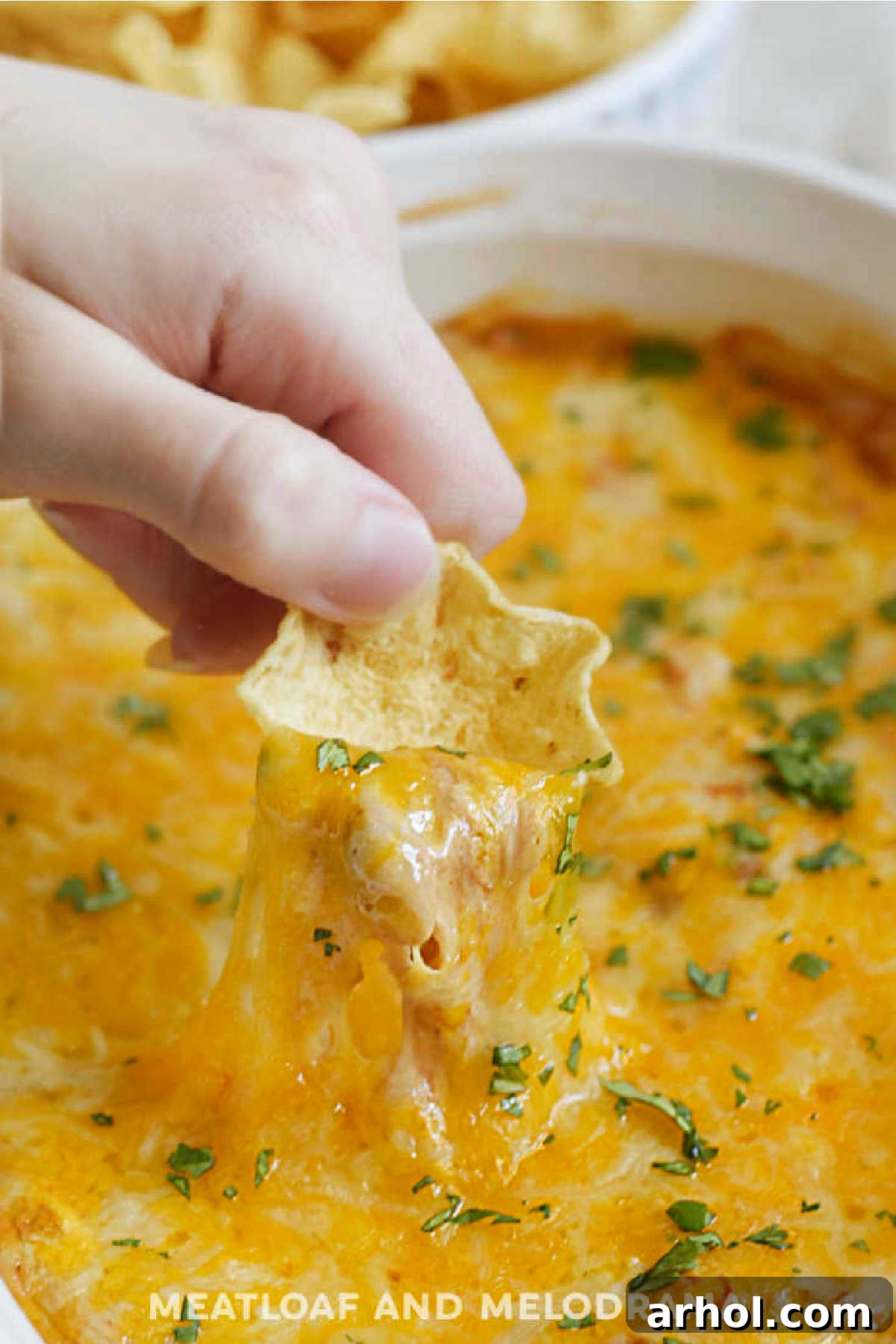 bean dip with gooey cheddar cheese pull on tortilla chip, showcasing a perfect scoop of the hot bean dip