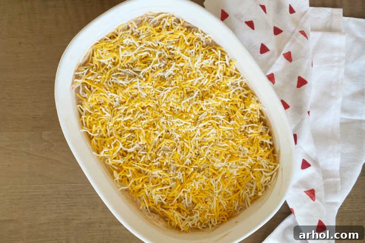 bean dip mixture with shredded cheese sprinkled on top in a white baking dish, ready for the oven