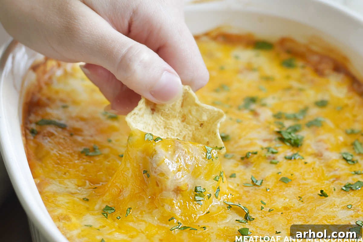 hand dipping tortilla chip into hot bean dip with melted cheese on top, showing a perfect scoop