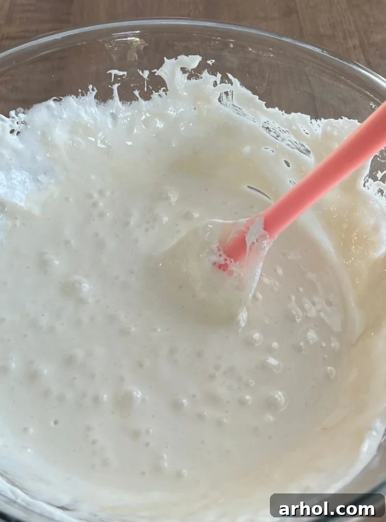 A large microwave-safe bowl with marshmallows and butter melting into a smooth, gooey mixture, ready for the next step of making Froot Loop Bars.