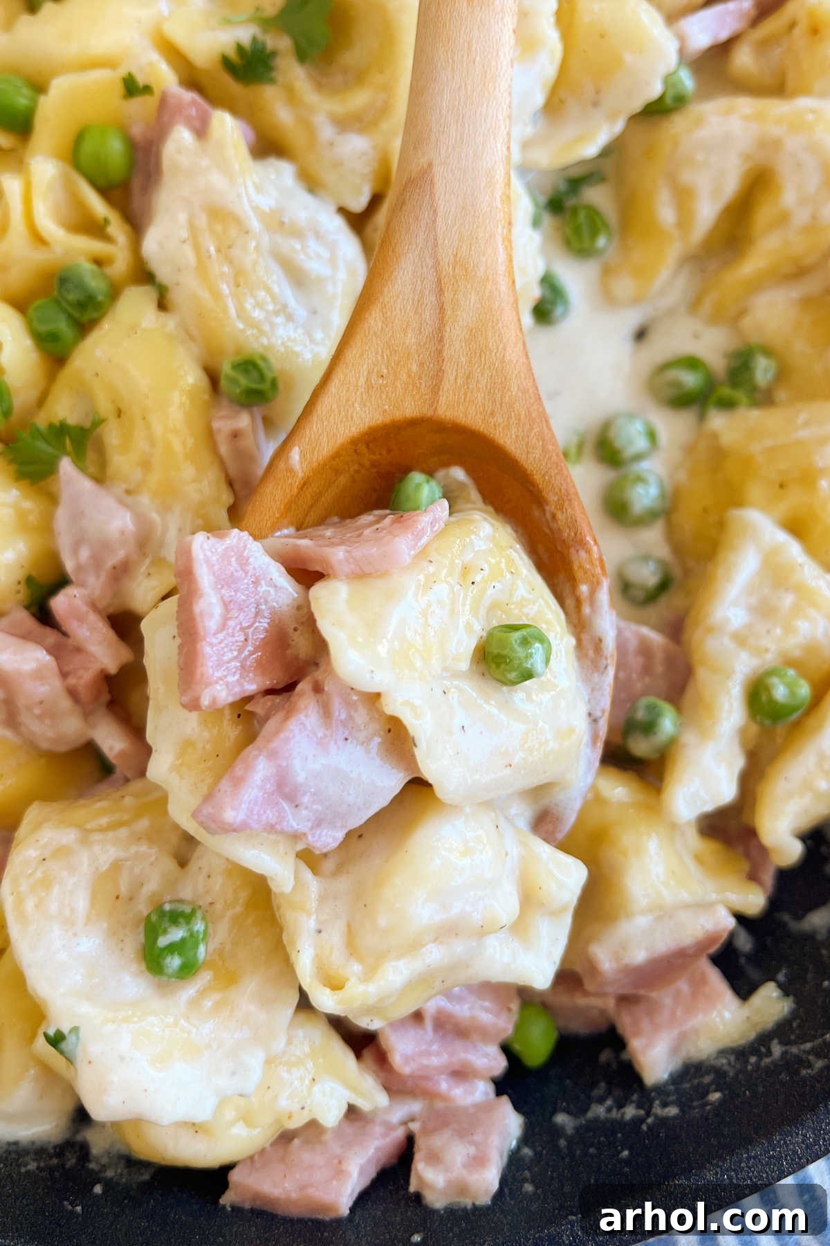 Creamy Cheese Tortellini with Ham and Peas in a Parmesan sauce, served on a wooden spoon